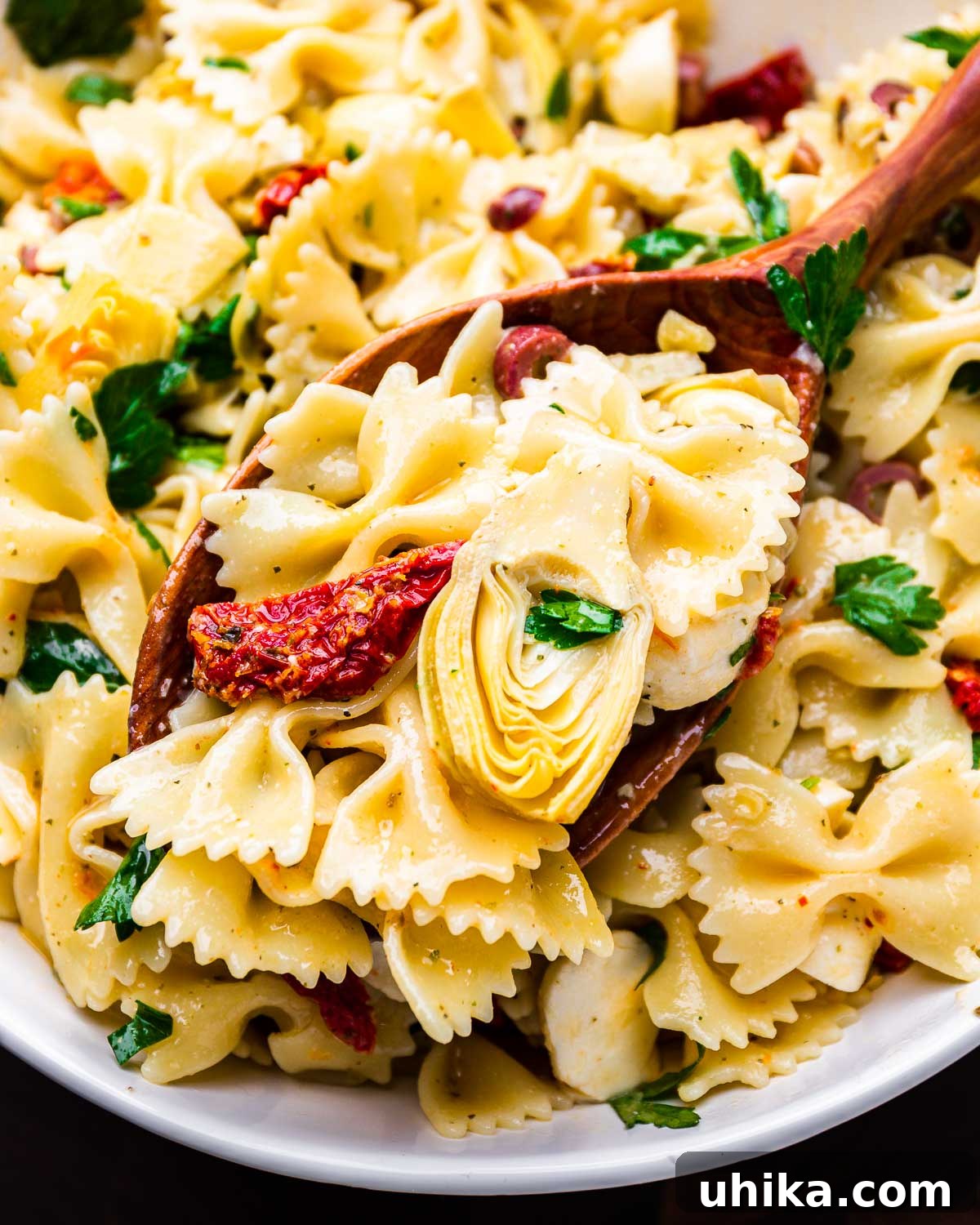 Mediterranean Sun-Dried Tomato and Artichoke Pasta Salad 2 Large spoon holding scoop of vibrant artichoke heart sun dried tomato pasta salad, showcasing bowtie pasta, mozzarella, and herbs. A perfect summer meal.