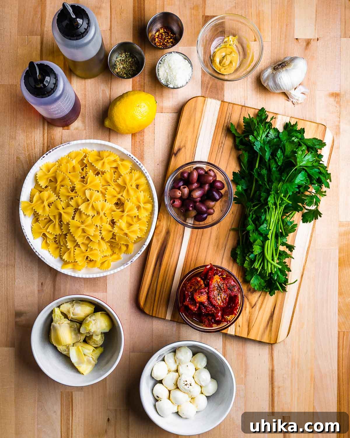Mediterranean Sun-Dried Tomato and Artichoke Pasta Salad 3 Collection of fresh ingredients for sun dried tomato artichoke pasta salad including bow tie pasta, sun-dried tomatoes, artichoke hearts, fresh mozzarella, olives, parsley, lemons, garlic, and oils. Ready for preparation.