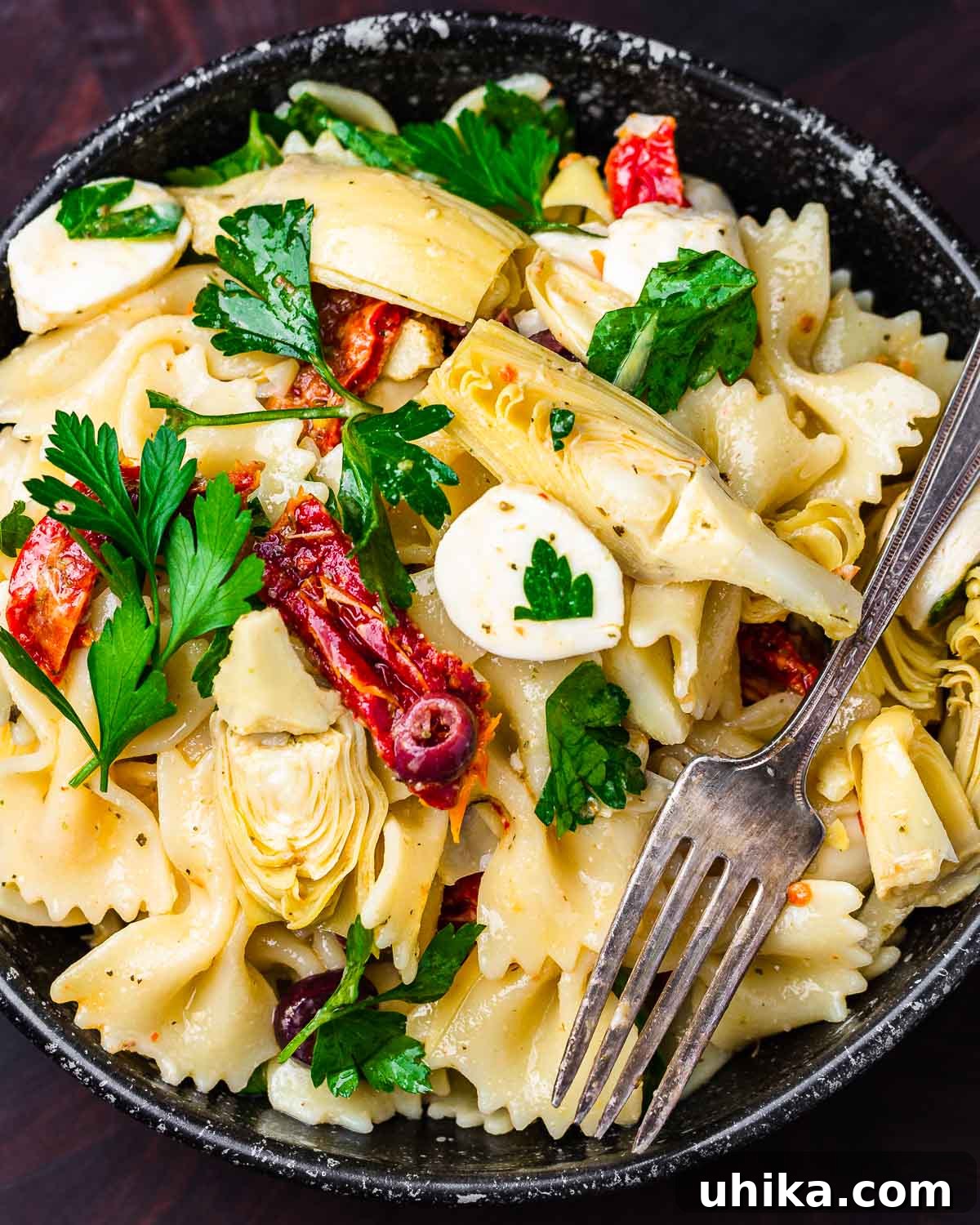 Mediterranean Sun-Dried Tomato and Artichoke Pasta Salad 7 Pasta salad with artichokes and sun dried tomatoes in black bowl, garnished with fresh parsley.
