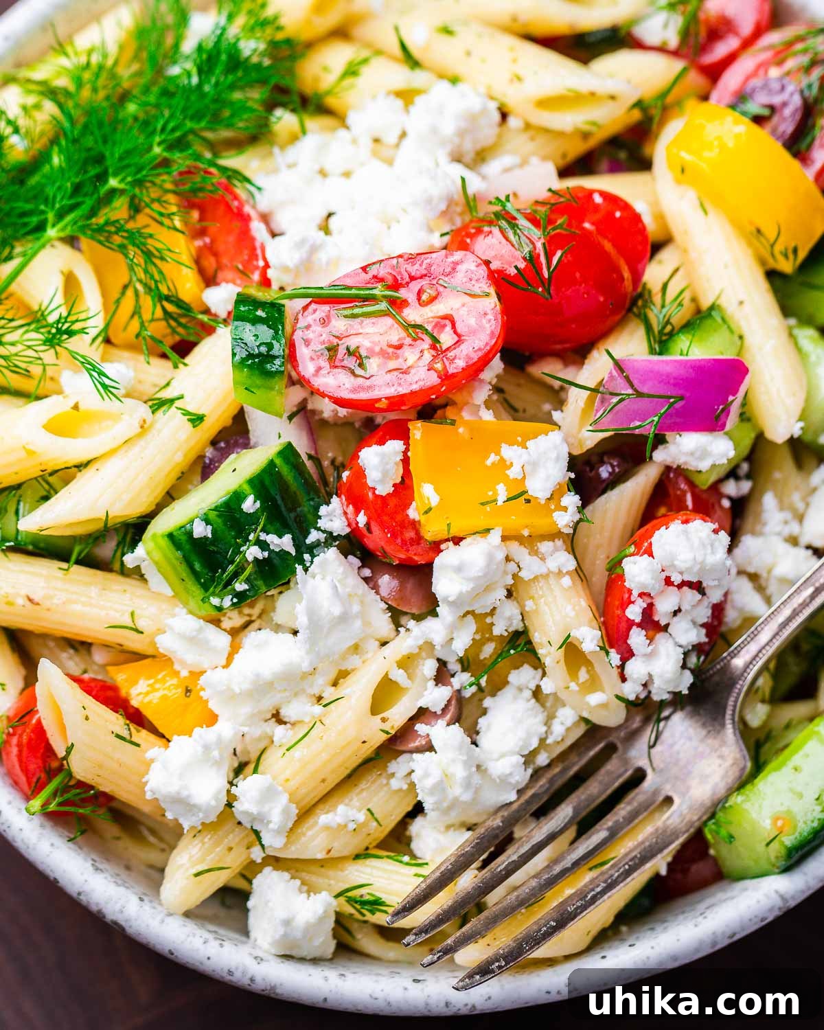Vibrant Mediterranean Pasta Salad 2 Closeup shot of Greek pasta salad in white bowl, highlighting fresh ingredients and textures.