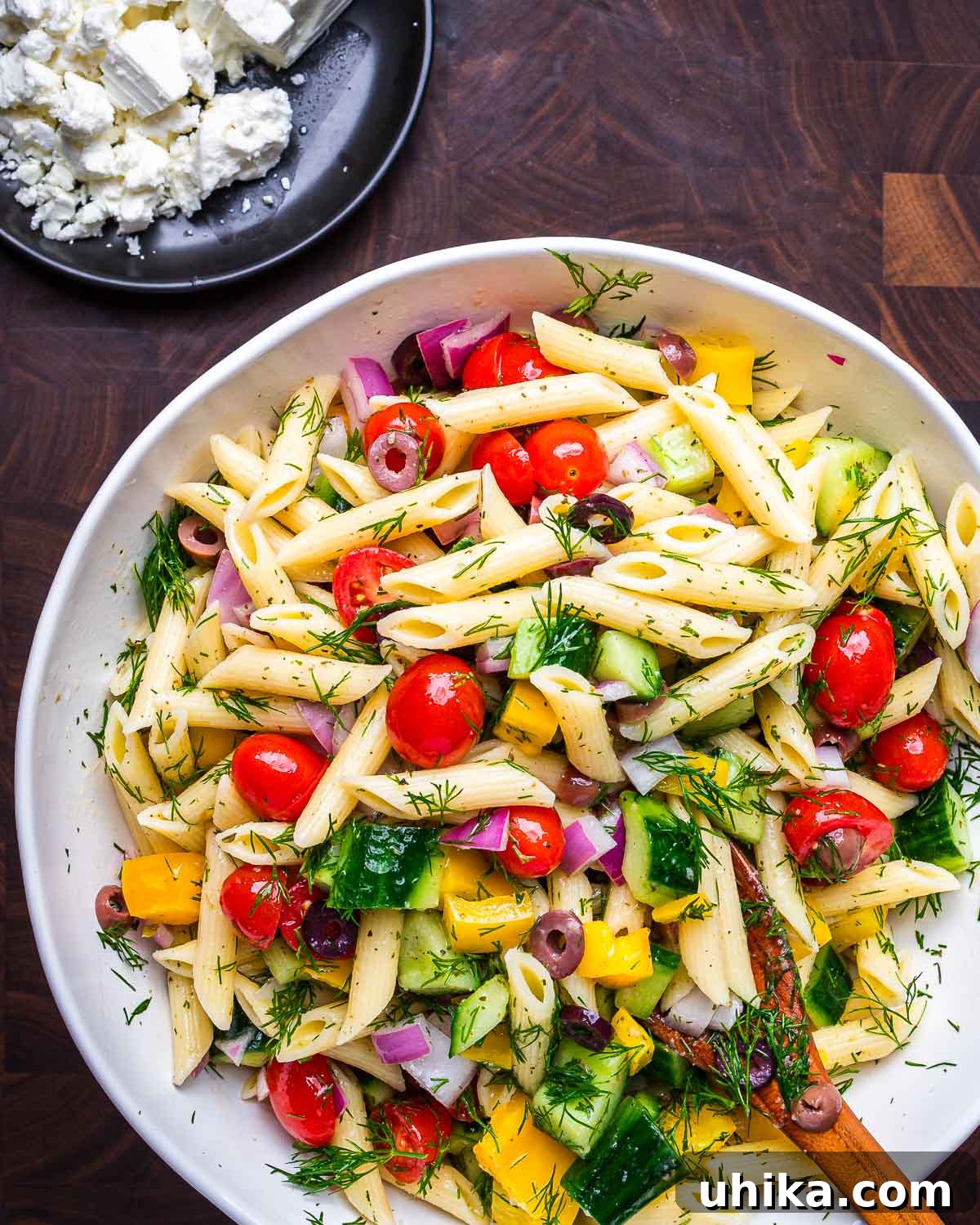 Vibrant Mediterranean Pasta Salad 5 Greek pasta salad in large serving bowl with a small plate of crumbled feta cheese on the side.