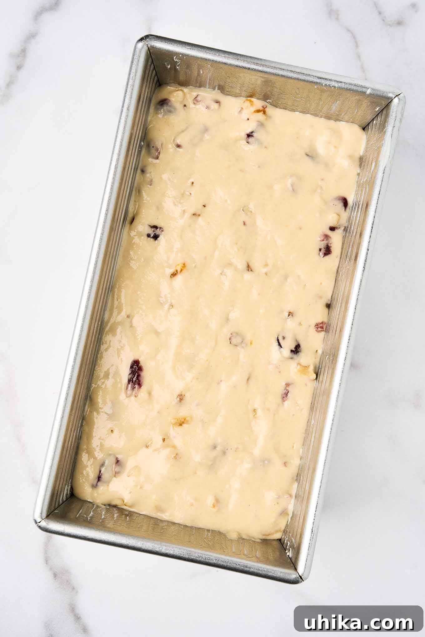 Sun-Kissed Apricot Cranberry Loaf 5 Unbaked batter for apricot quick bread with cranberries and walnuts spread evenly in a greased metal loaf pan, ready for the oven.
