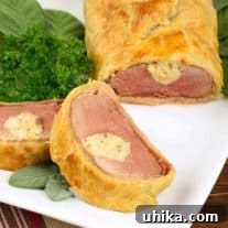 Cheese-stuffed pork tenderloin wrapped in golden puff pastry, served on a white plate garnished with fresh herbs.