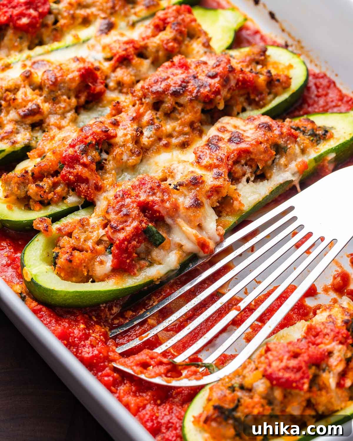 Sausage Stuffed Zucchini Bake 2 Sausage stuffed zucchini boats in white baking dish with spatula.