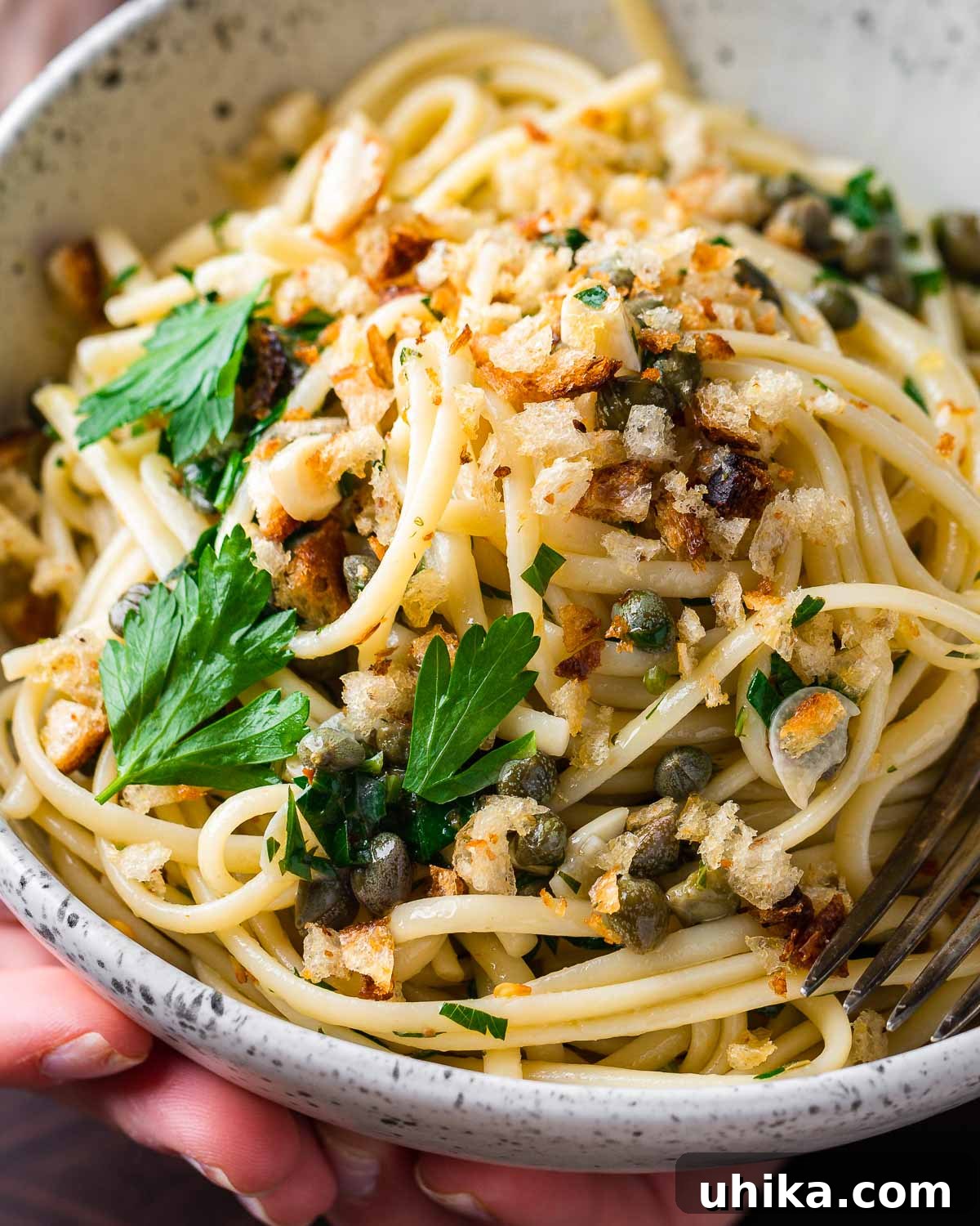 Zesty Lemon Caper Pasta 10 Hands holding lemon caper pasta in white bowl.