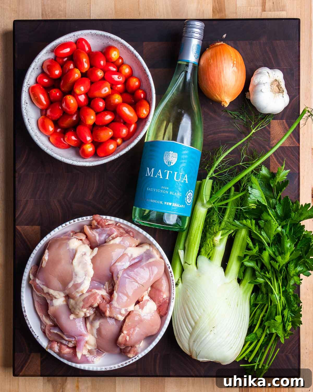 Golden Chicken Thighs with Roasted Fennel and Burst Tomatoes 4 A flat lay of fresh ingredients: cherry tomatoes, white wine, sliced onion, garlic cloves, boneless chicken thighs, and a whole fennel bulb.