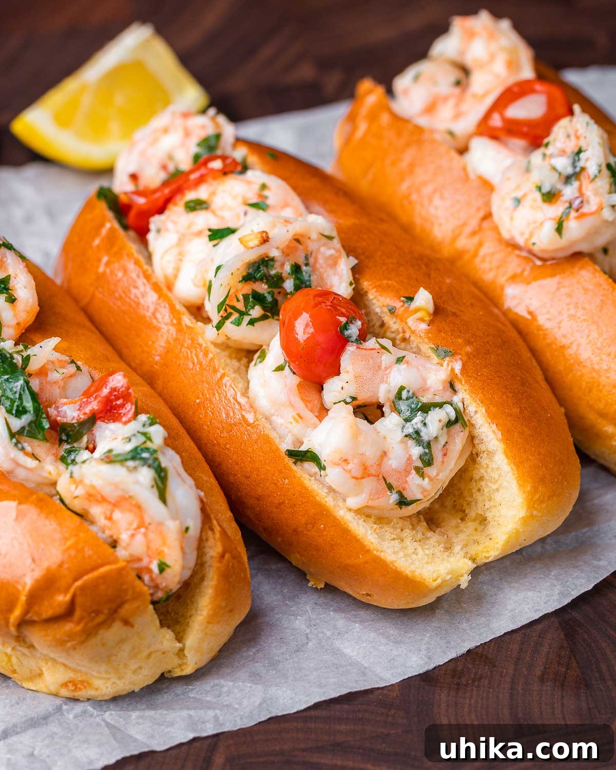 Three perfectly assembled shrimp scampi rolls on paper, garnished with fresh herbs and lemon wedges.