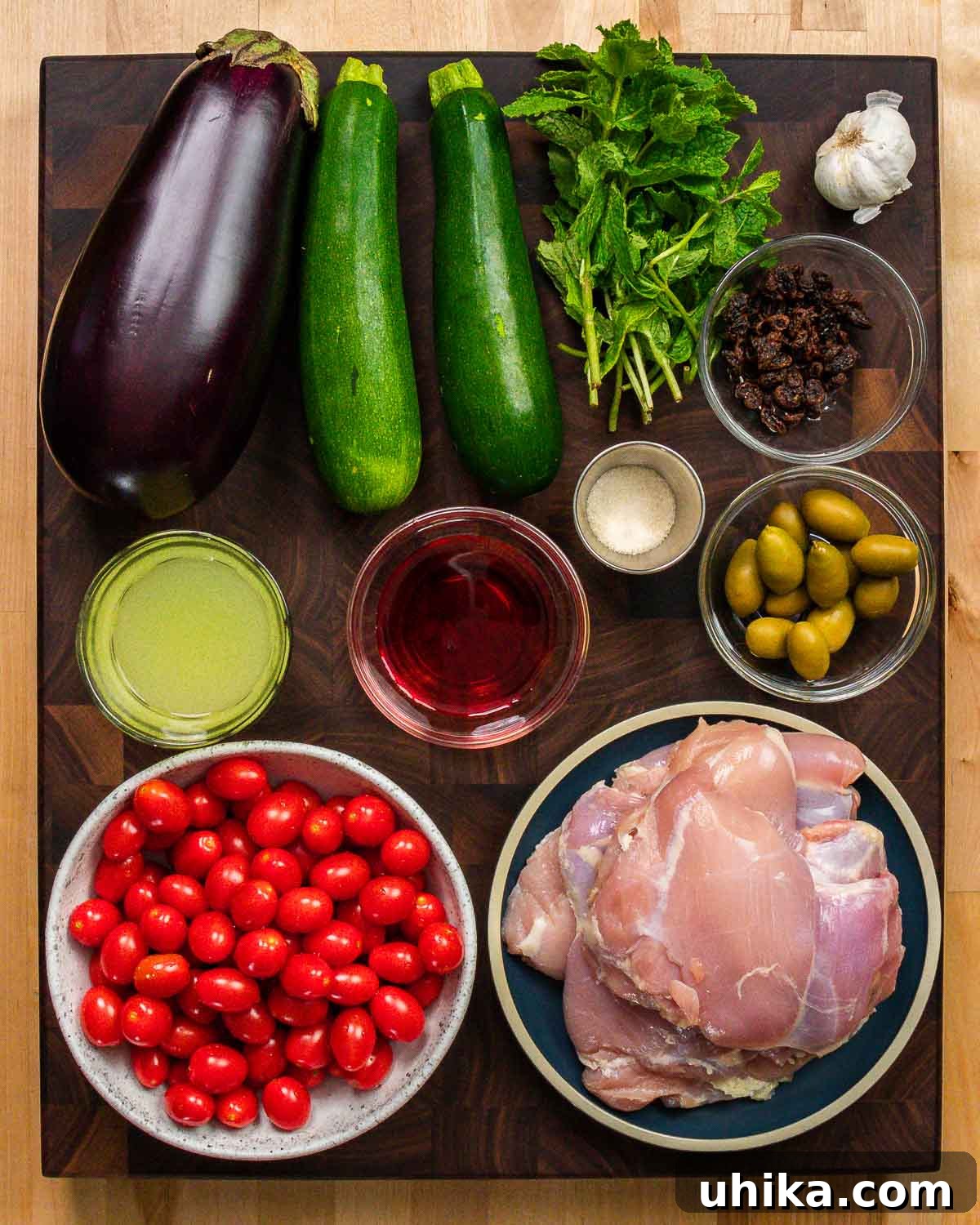 Sicilian Agrodolce Chicken 3 A vibrant display of fresh ingredients for Chicken Agrodolce, including eggplant, zucchini, mint, garlic, raisins, sugar, chicken stock, vinegar, olives, tomatoes, and boneless chicken thighs.