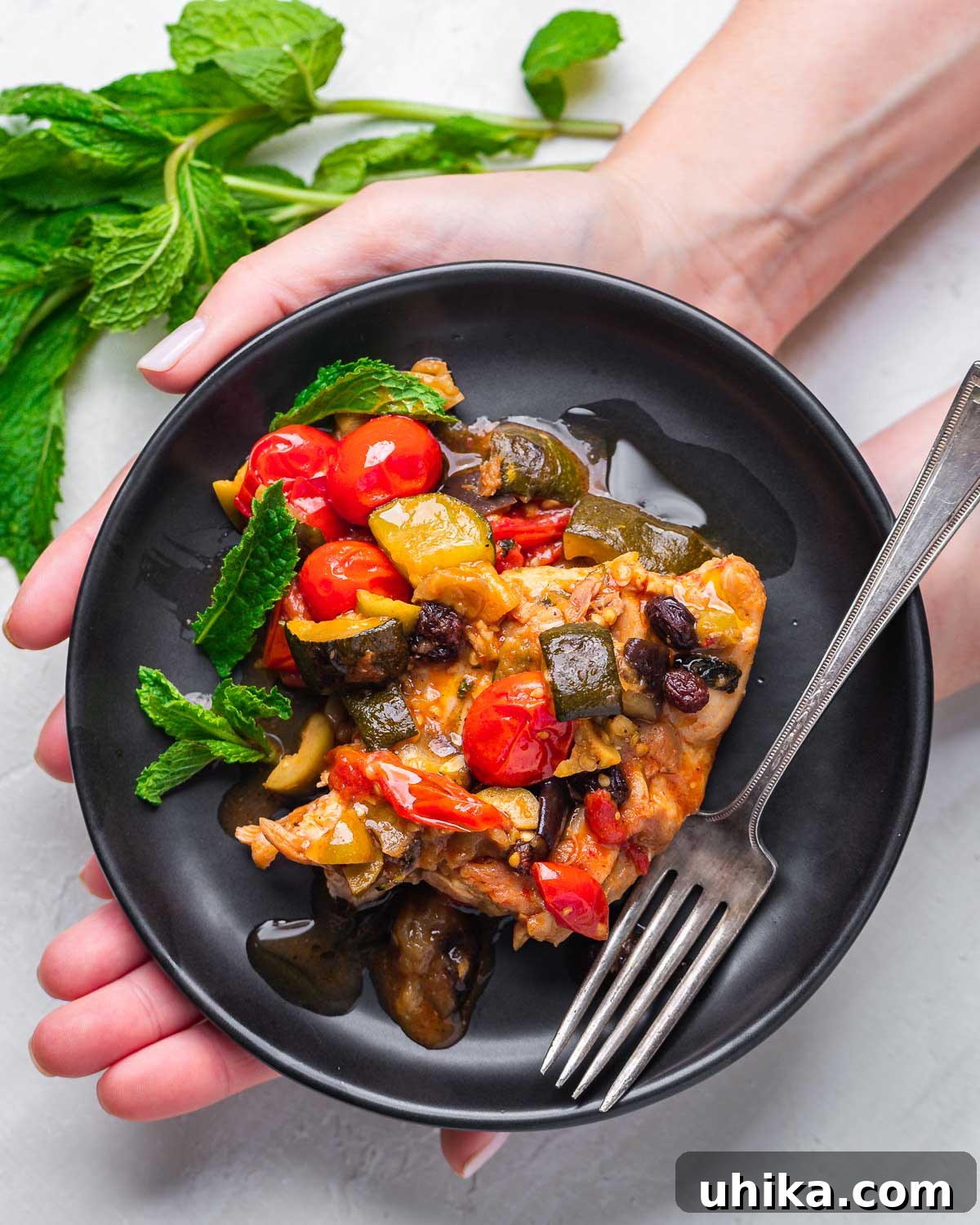 Sicilian Agrodolce Chicken 8 Hands holding a black plate with a generous serving of Chicken Agrodolce, ready to be enjoyed.