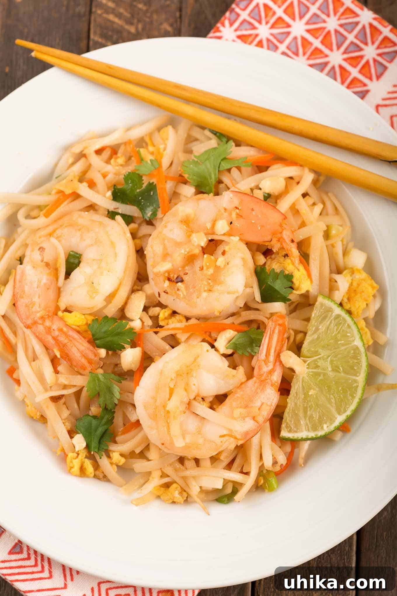 A single serving of shrimp pad Thai on a white plate with a lime wedge and chopsticks.