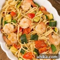An overhead view of an oval casserole filled with sautéed zucchini and red bell pepper tossed in a light garlic sauce with linguine and shrimp.