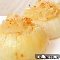 A white plate with two baked stuffed Vidalia onions filled with a creamy, sautéed onion mixture and topped with golden breadcrumbs.