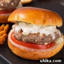 A serving board with a grilled lamb burger on a brioche bun with tzatziki sauce and slices of onion and tomato.