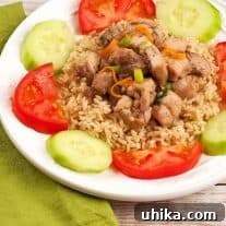 Sweet five-spice ginger chicken served over brown rice, garnished with tomato wedges and cucumber slices on a white plate.