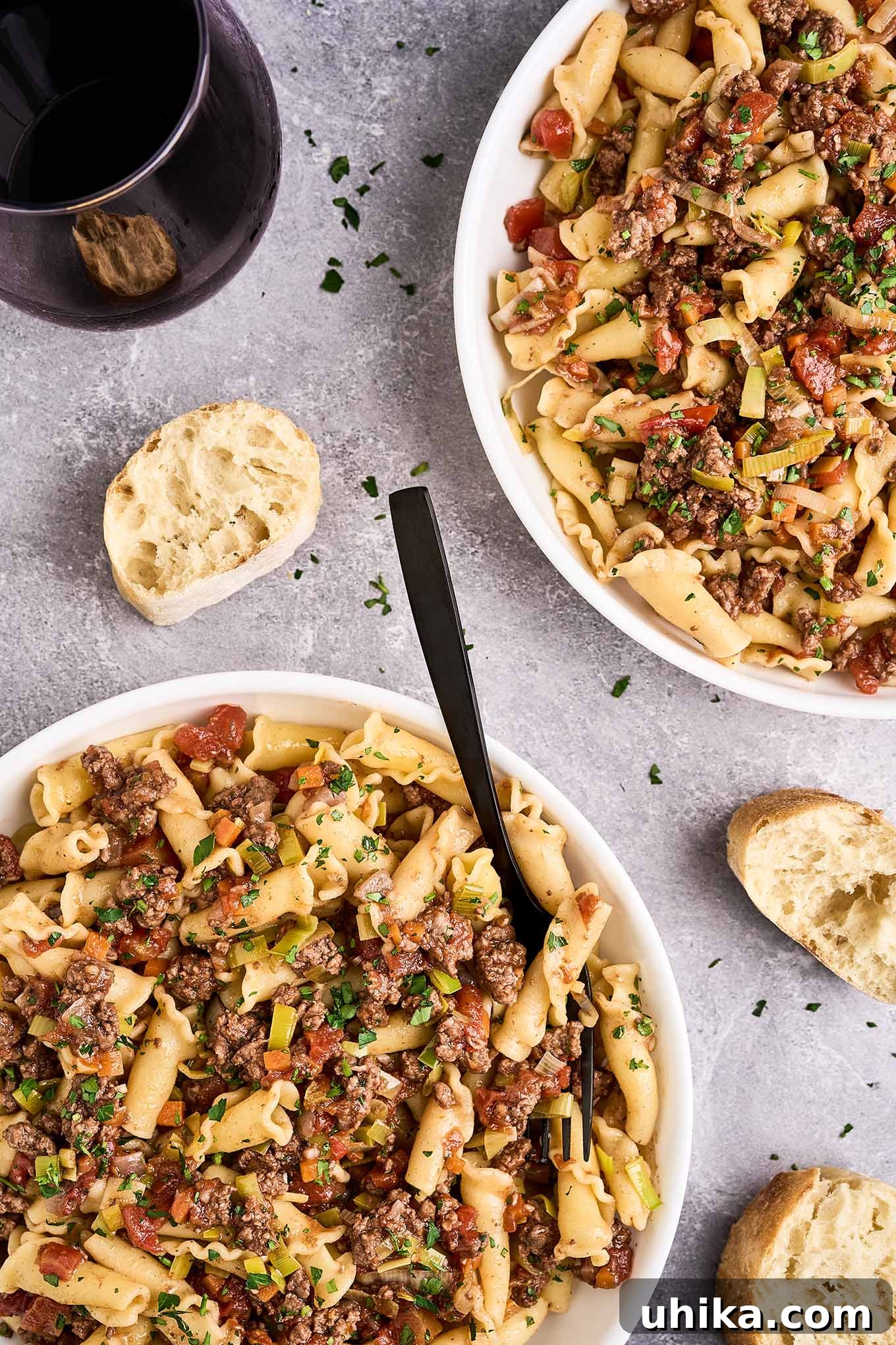 Effortless Ground Lamb Ragu 2 An overhead view of two bowls of lamb ragu with pasta, slices of crusty baguette, and a glass of red wine.