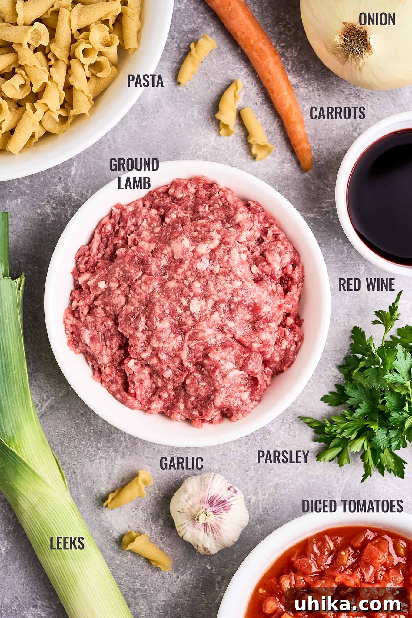 Effortless Ground Lamb Ragu 3 A labeled, overhead view of the ingredients needed to make lamb ragu; ground lamb, pasta, onion, garlic, carrot, parsley, leeks, red wine, and diced tomatoes.