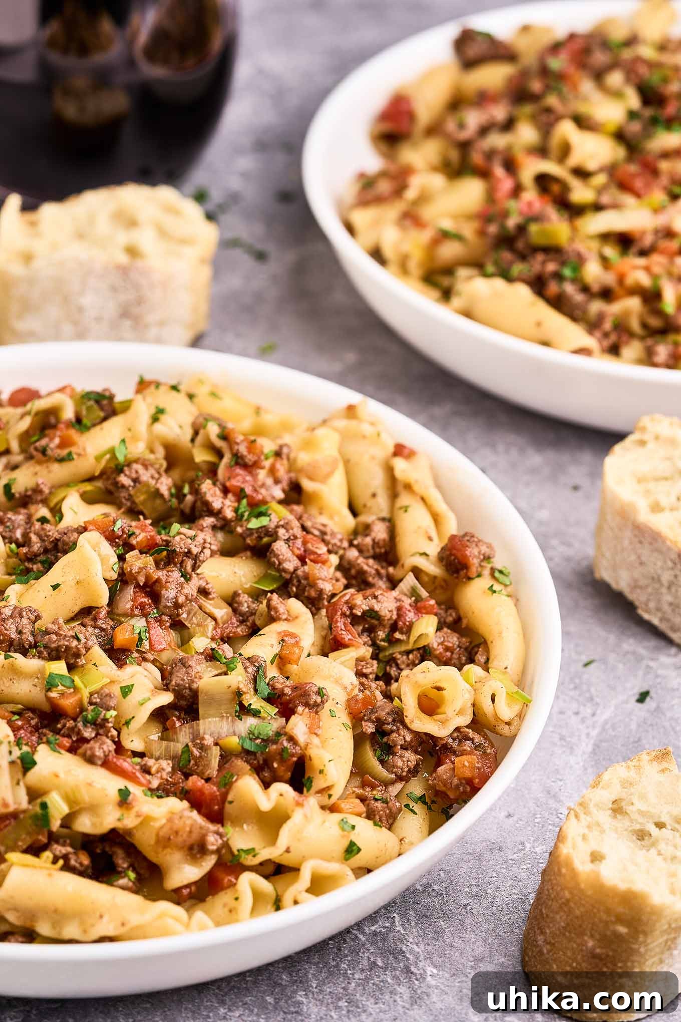 Effortless Ground Lamb Ragu 4 A serving of lamb ragu over pasta in a shallow bowl showing sliced leeks, diced tomatoes, carrots, and parsley in the ragu - red wine in the background.