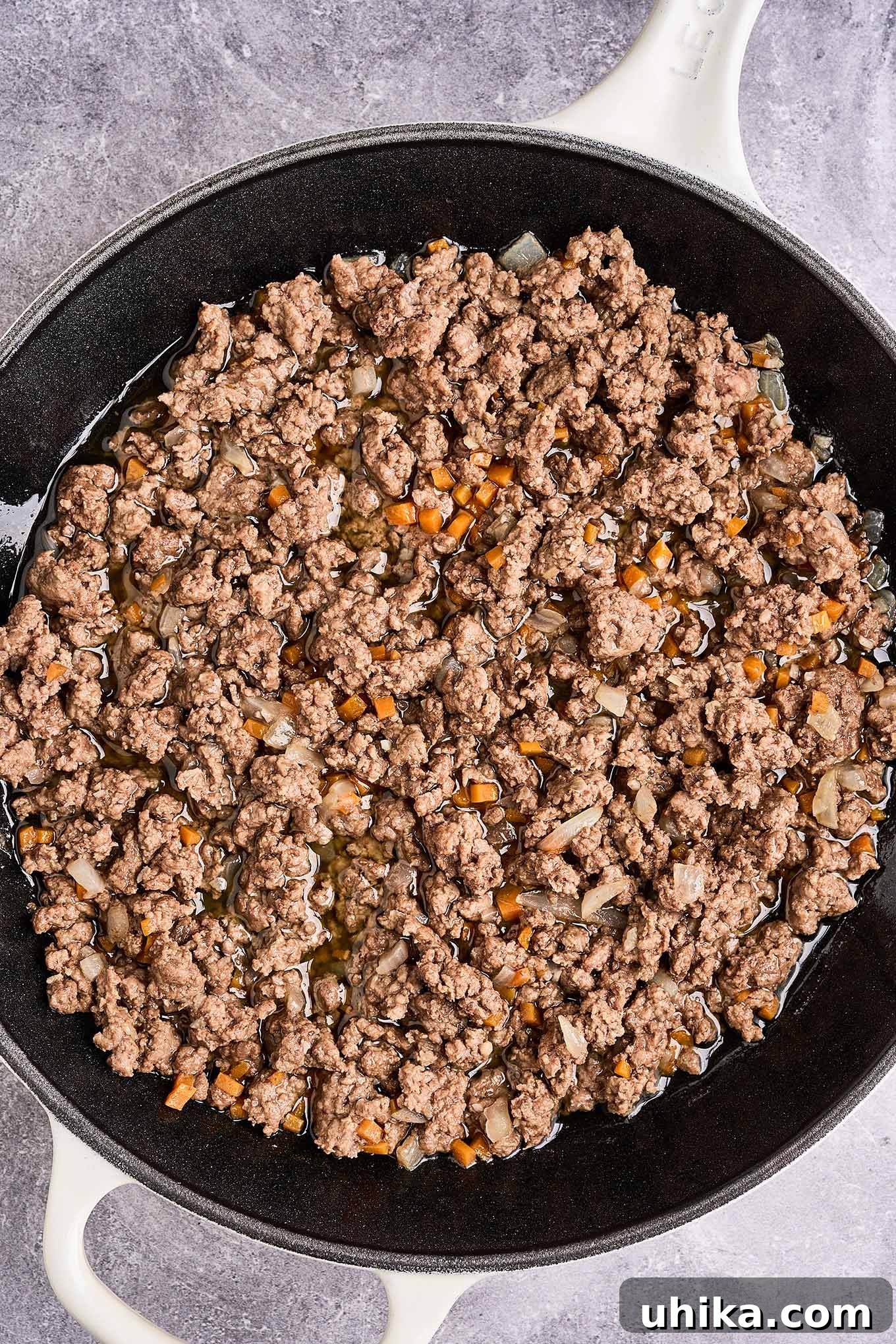 Effortless Ground Lamb Ragu 5 A cast iron pan filled with ground lamb sautéed with onion, garlic, and chopped carrot, ready to be drained of fat and combined with other ingredients.