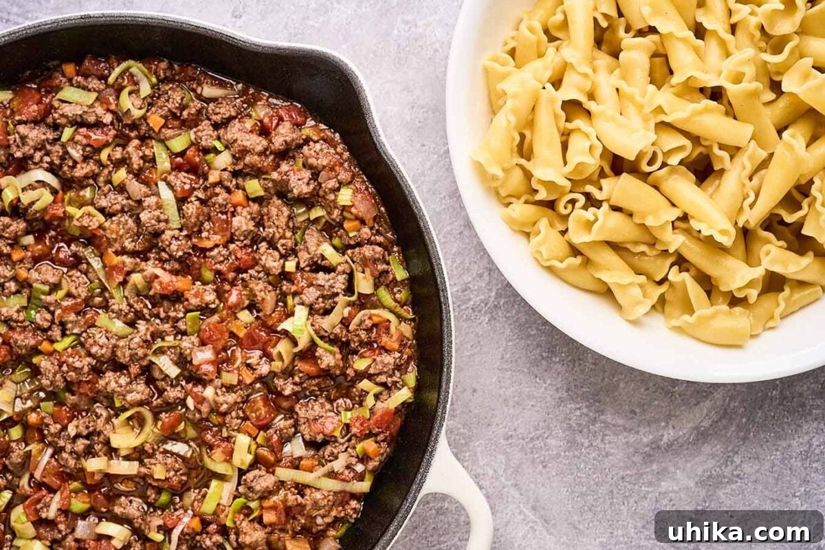 Effortless Ground Lamb Ragu 7 Finished lamb ragu in a cast iron pan with a bowl of cooked campanelle pasta next to the right, ready to be combined and served.