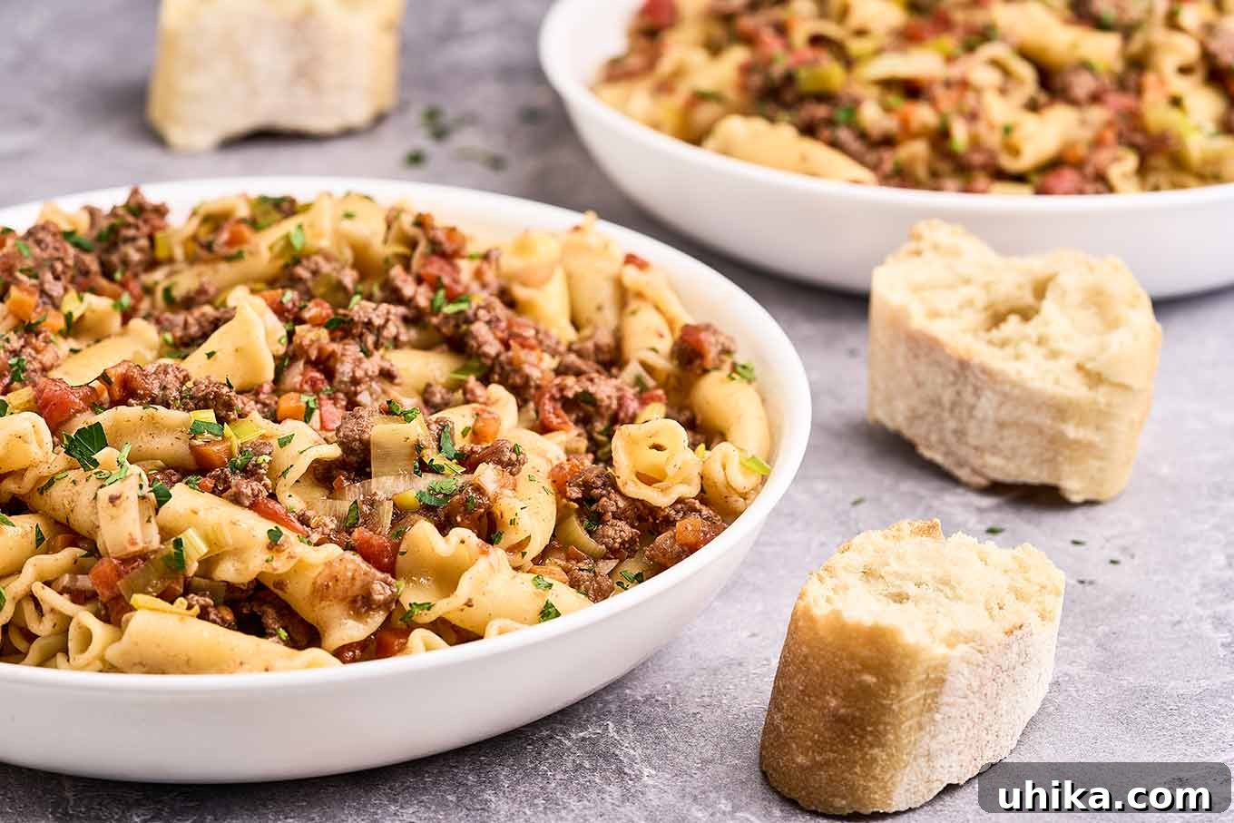 Effortless Ground Lamb Ragu 8 A close view of a shallow pasta bowl filled with ground lamb ragu and campanelle pasta, a second bowl and slices of baguette to the rear and side.