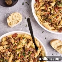 An overhead view of two bowls of lamb ragu with pasta, slices of crusty baguette, and a glass of red wine.