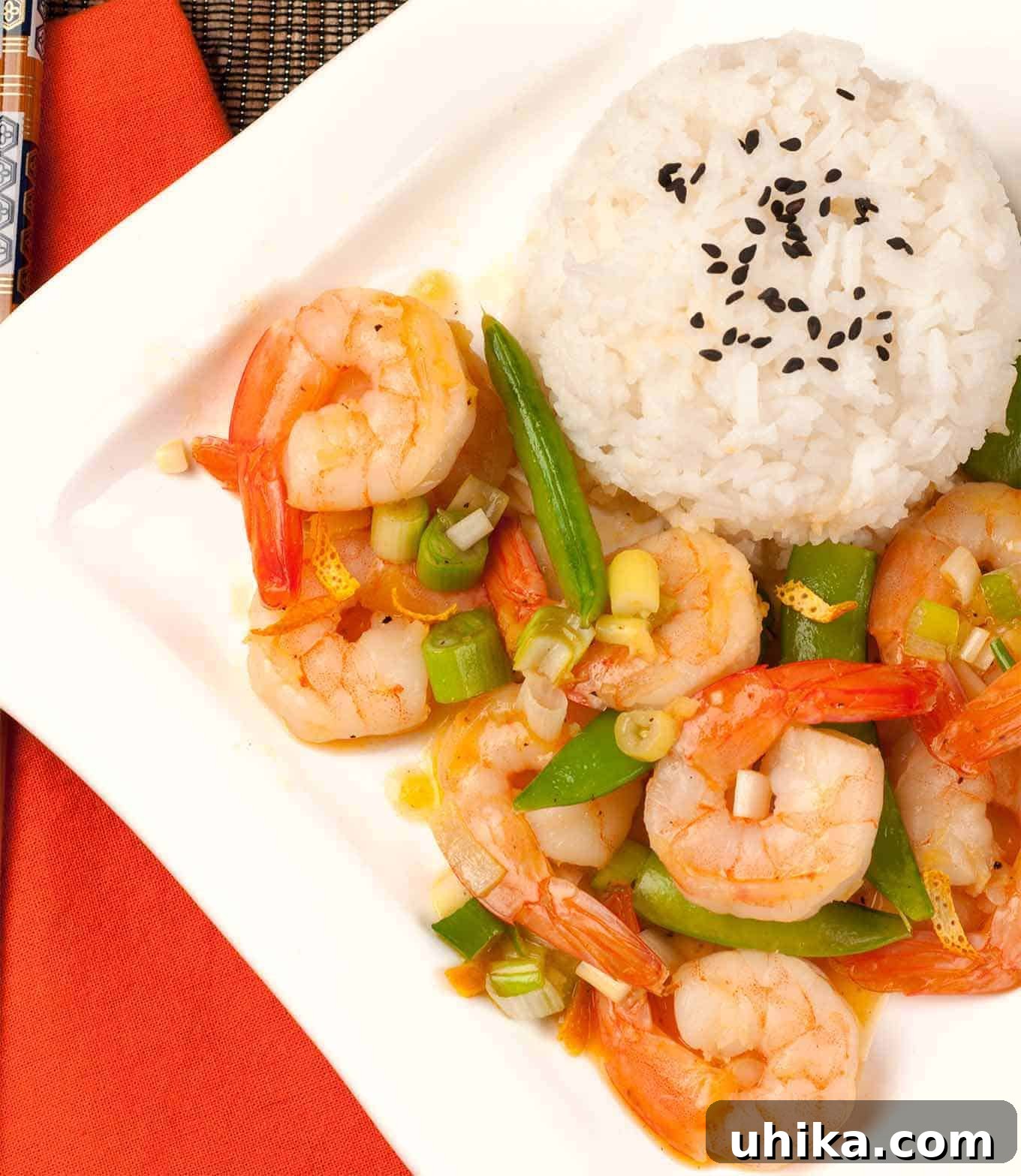 Zingy Orange Shrimp Stir-Fry 2 An overhead view of stir-fried shrimp with orange peel, snap peas, and scallions served with white rice topped with black sesame seeds, showcasing a vibrant and healthy meal.
