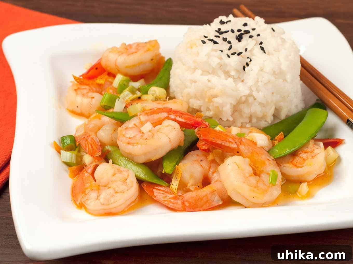 Zingy Orange Shrimp Stir-Fry 3 A side view of stir-fried shrimp with orange peel, snap peas, and scallions served with white rice topped with black sesame seeds, highlighting the textures and colors.