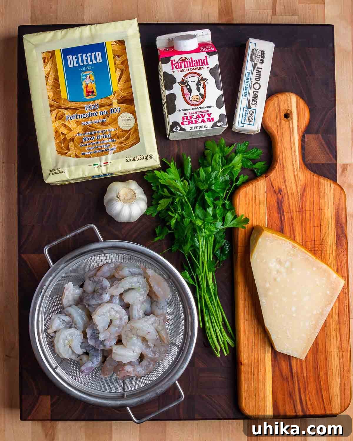 Decadent Shrimp Alfredo Pasta 4 Ingredients laid out for Shrimp Alfredo: fettuccine pasta, heavy cream, unsalted butter, minced garlic, raw shrimp, fresh parsley, and grated Parmigiano Reggiano cheese.