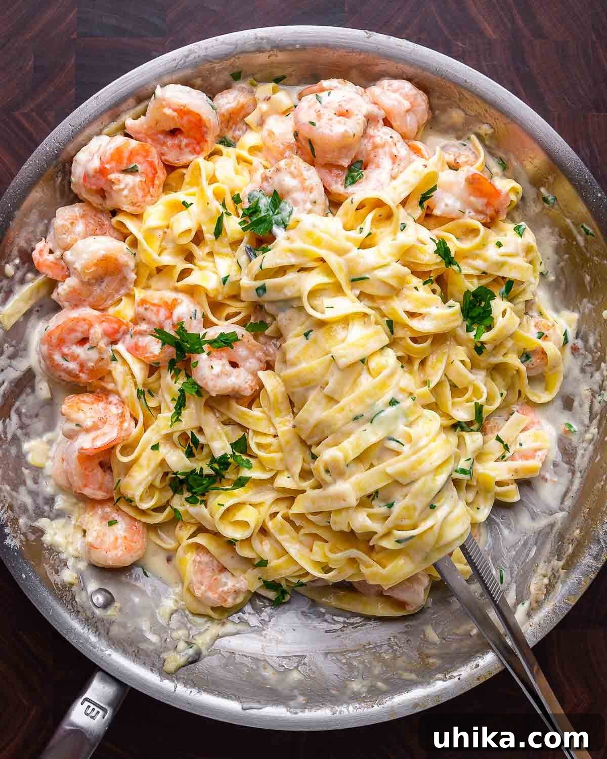 Decadent Shrimp Alfredo Pasta 7 Shrimp Alfredo served in a stainless steel pan on a rustic wooden cutting board.