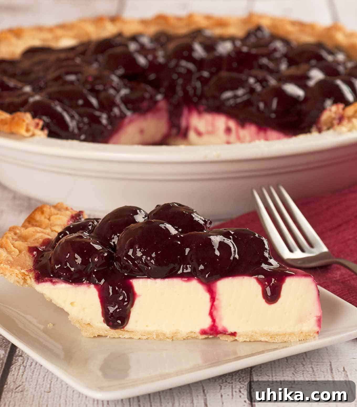Tangy Fruit Greek Yogurt Delight 2 A dessert plate with a slice of Greek yogurt pie topped with fresh cherry topping, the remainder of the pie in a white pie plate in the background. A perfect summer treat.