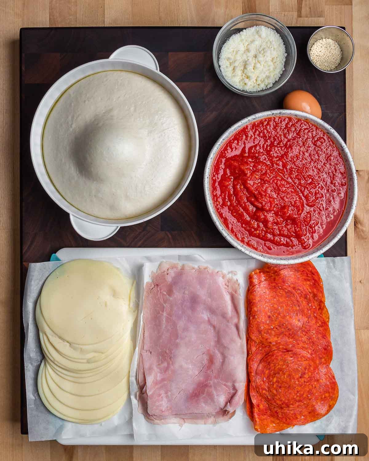 Mount Stromboli 3 Ingredients for Stromboli laid out: pizza dough, Pecorino cheese, sesame seeds, one egg, marinara sauce, sliced provolone, sliced ham, and sliced pepperoni.