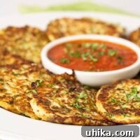 A serving platter of freshly made zucchini fritters garnished with chopped parsley and arranged around a small round bowl of marinara dipping sauce.