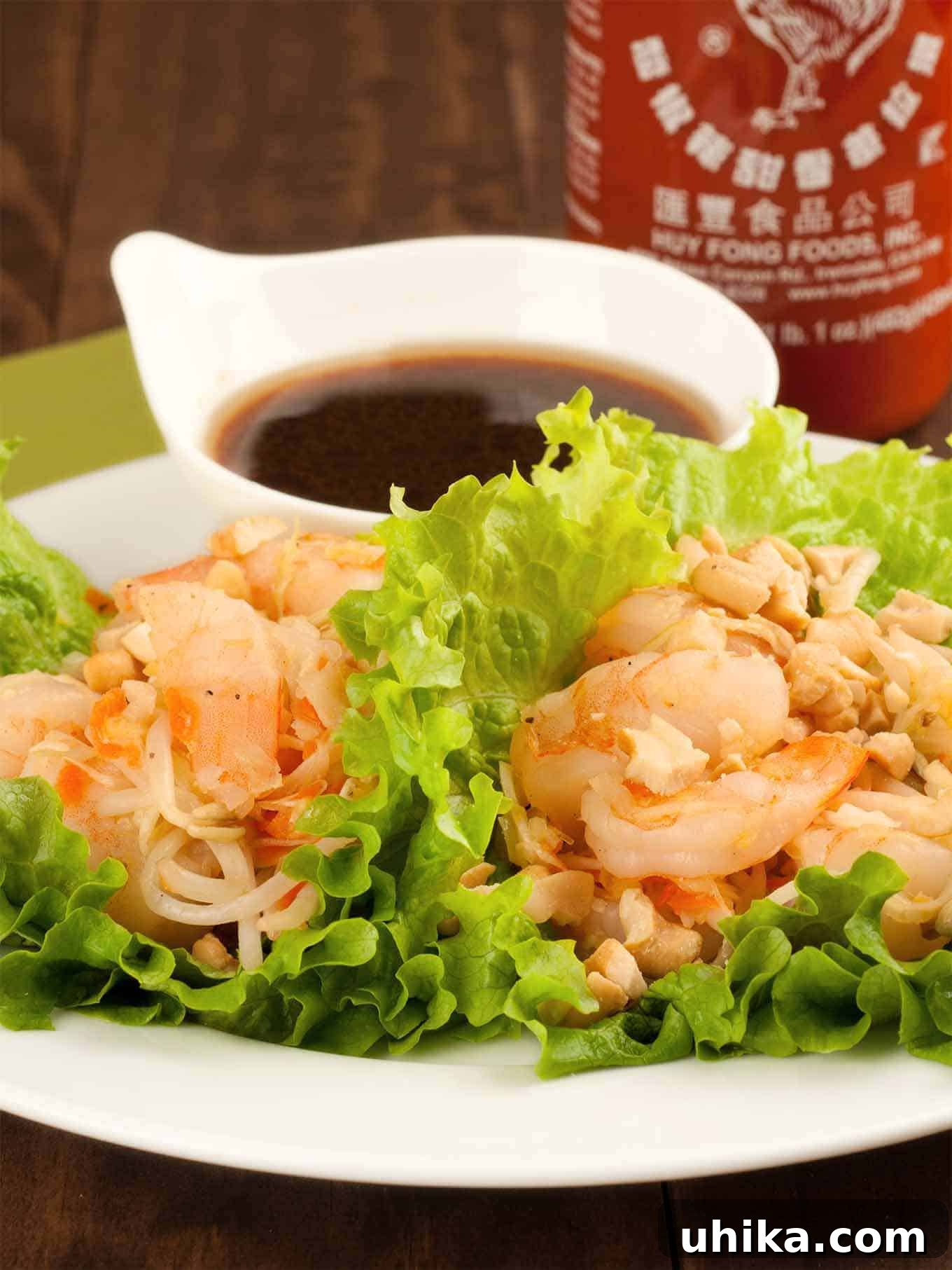 Firecracker Shrimp Lettuce Cups 2 A vibrant plate of sweet and spicy shrimp lettuce wraps, generously filled with succulent shrimp, crunchy chopped peanuts, and delicate noodles, beautifully arranged and served alongside a small bowl of savory dipping sauce.