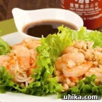 A plate of sweet and spicy shrimp lettuce wraps filled with shrimp, chopped peanuts, and noodles, served with dipping sauce.