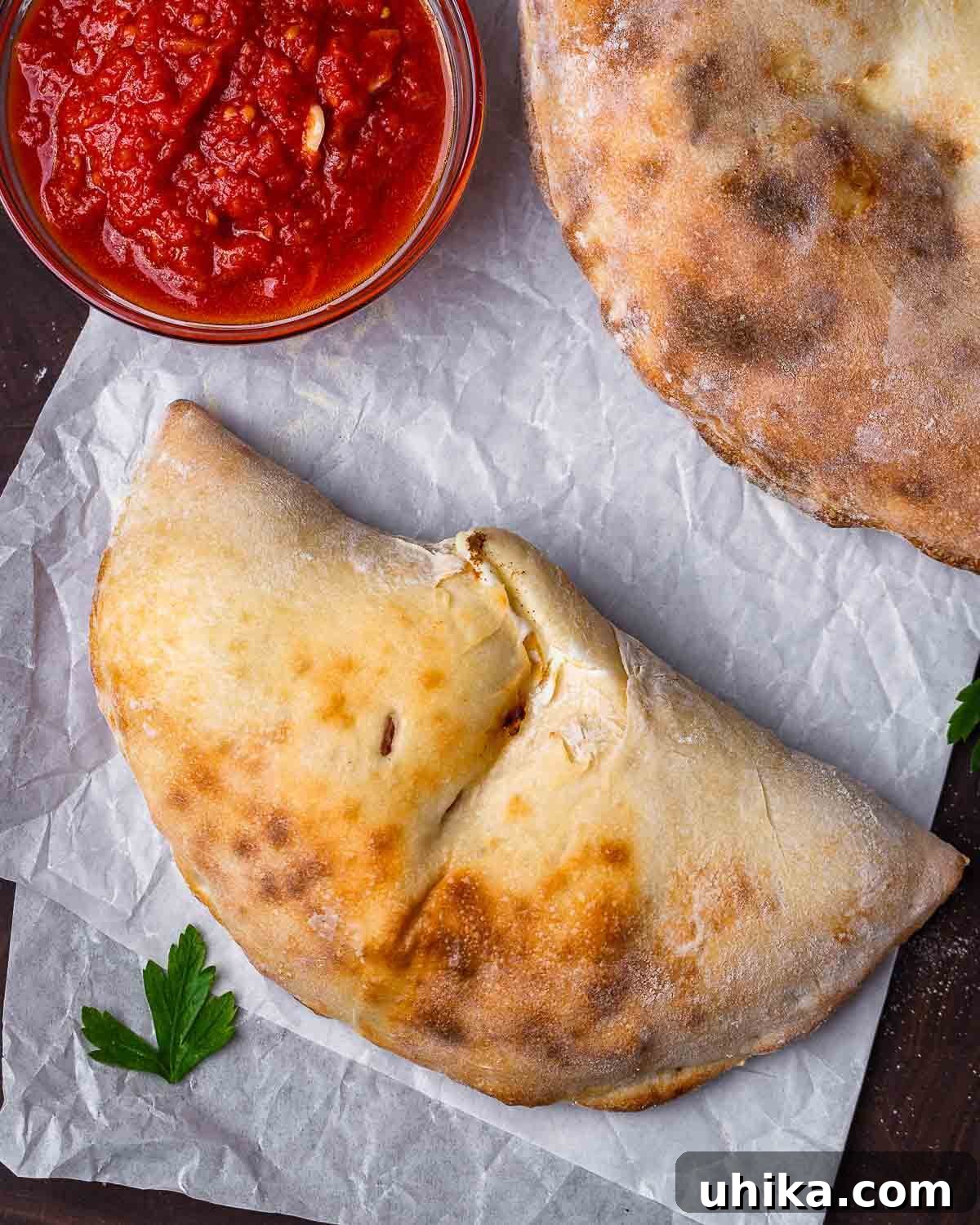 Overhead shot of two golden-brown calzones and a small bowl of rich marinara sauce, ready for dipping.
