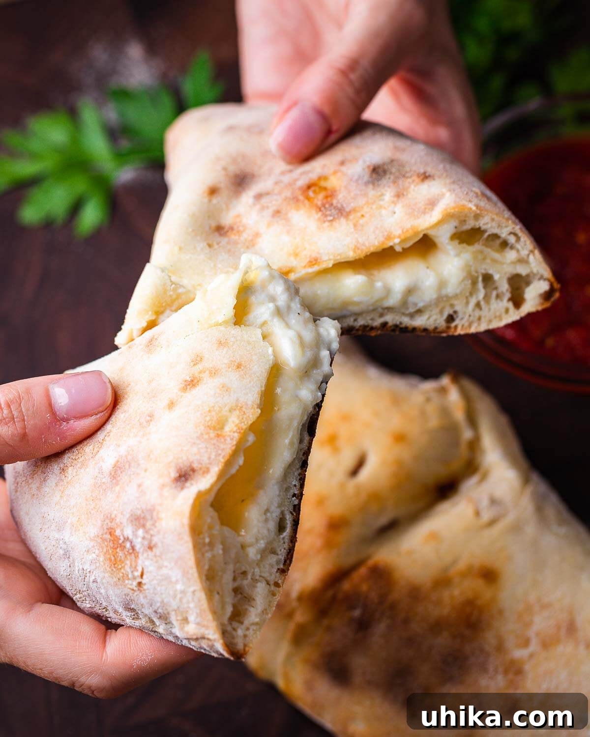 Hands holding a freshly cut in half calzone, revealing the melted cheese filling.