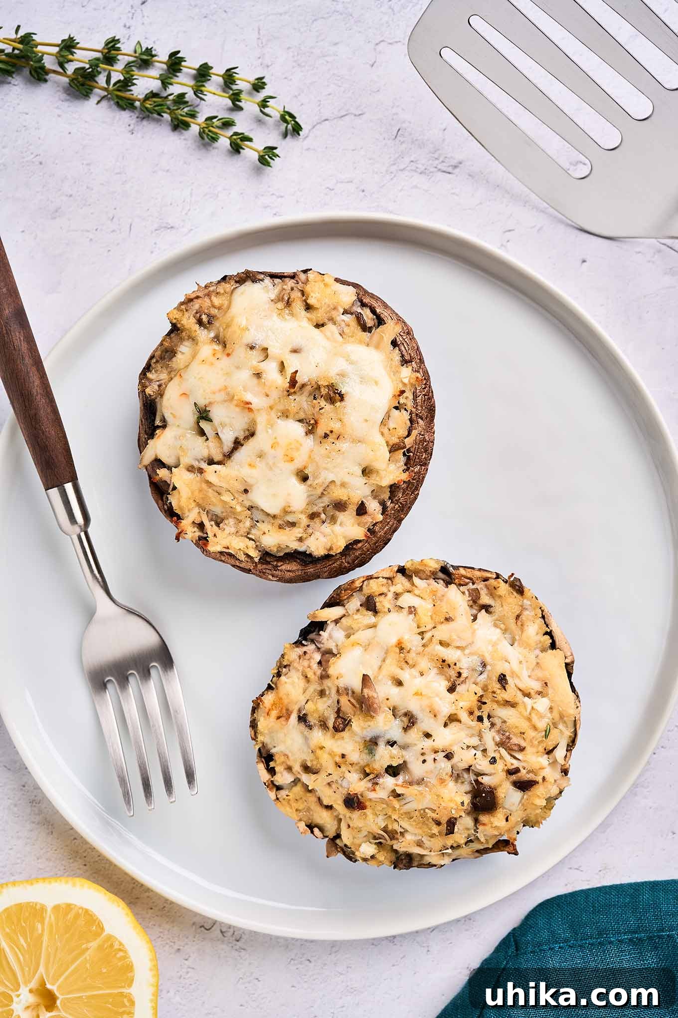 Elegant Crab Stuffed Portobello Caps 2 Freshly baked crab-stuffed portobello mushrooms with a golden-brown cheese topping, served on a round white plate with a dinner fork and a lemon wedge garnish, highlighting an exquisite seafood dish.