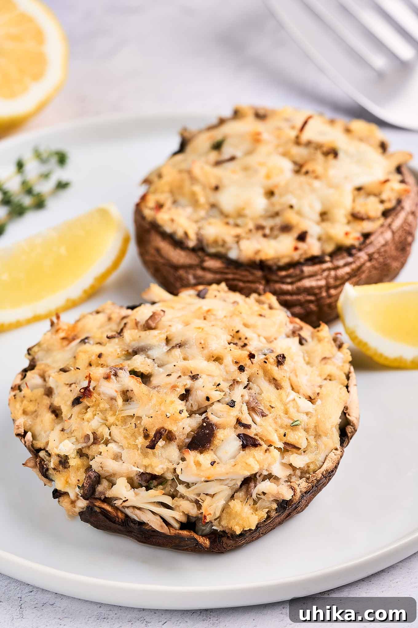 Elegant Crab Stuffed Portobello Caps 6 A perfectly plated dish of crab-stuffed portobello mushrooms, showcasing melted cheese, fresh lemon wedges, and thyme sprigs, ready for an elegant serving.
