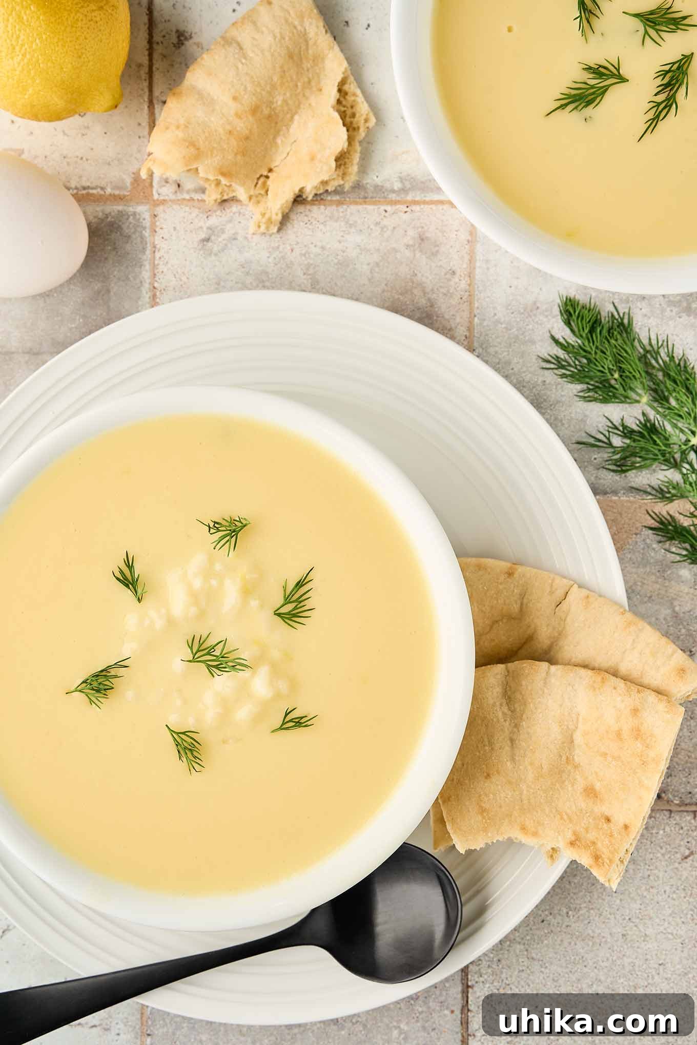 Golden Greek Avgolemono Soup 2 Silky Greek egg and lemon soup, Avgolemono, garnished with fresh dill, served with warm pita bread in a white bowl.