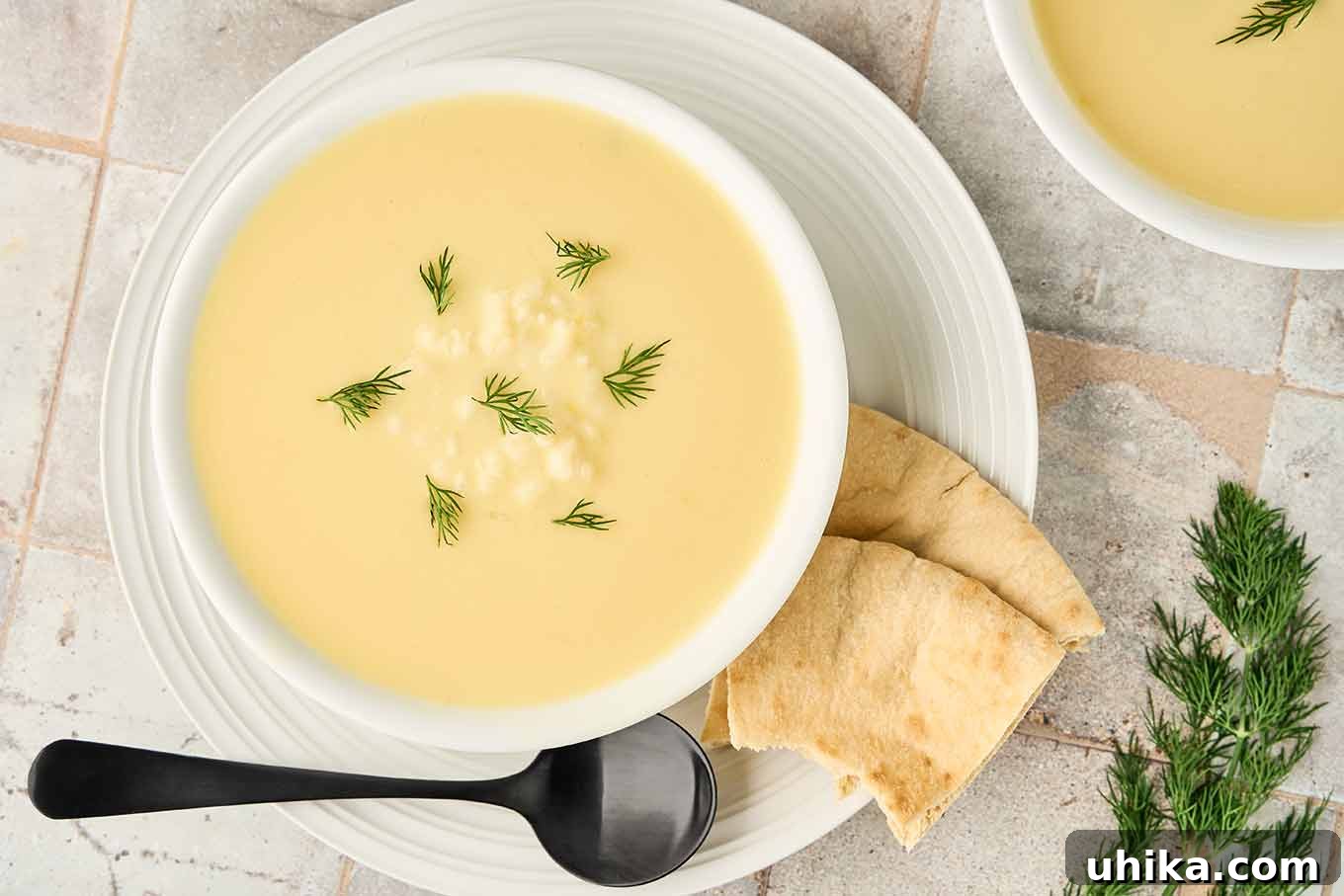 Golden Greek Avgolemono Soup 7 Beautifully plated Greek egg and lemon soup, Avgolemono, garnished with fresh dill, served in a white bowl with a side of toasted pita bread, ready to be enjoyed.