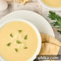 Greek egg and lemon soup, Avgolemono, garnished with fresh dill, served with warm pita bread and a soup spoon on a white plate.