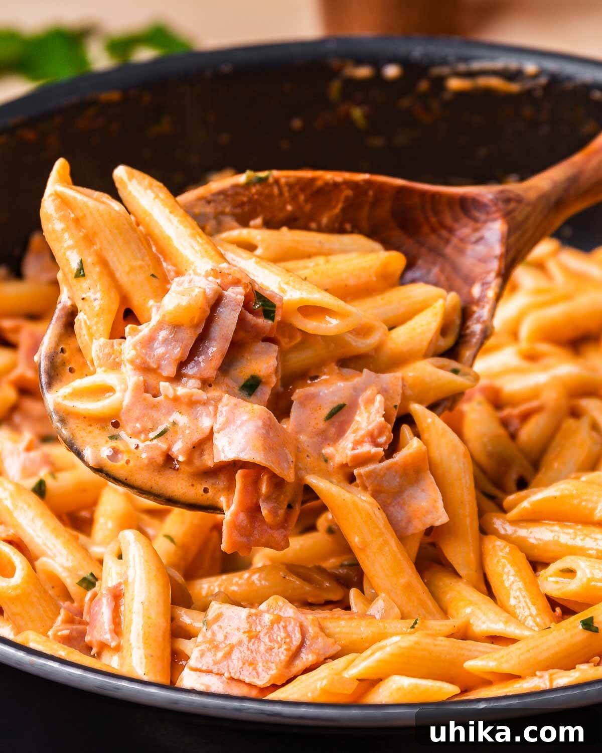 Wooden spoon lifting a portion of Penne al Baffo with ham and creamy sauce.