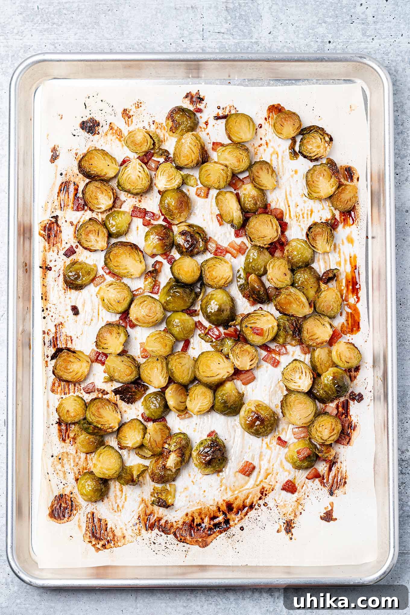 Sticky Maple Bacon Brussels Sprouts 5 Fully cooked maple glazed Brussels sprouts on a parchment lined baking sheet with bacon bits.