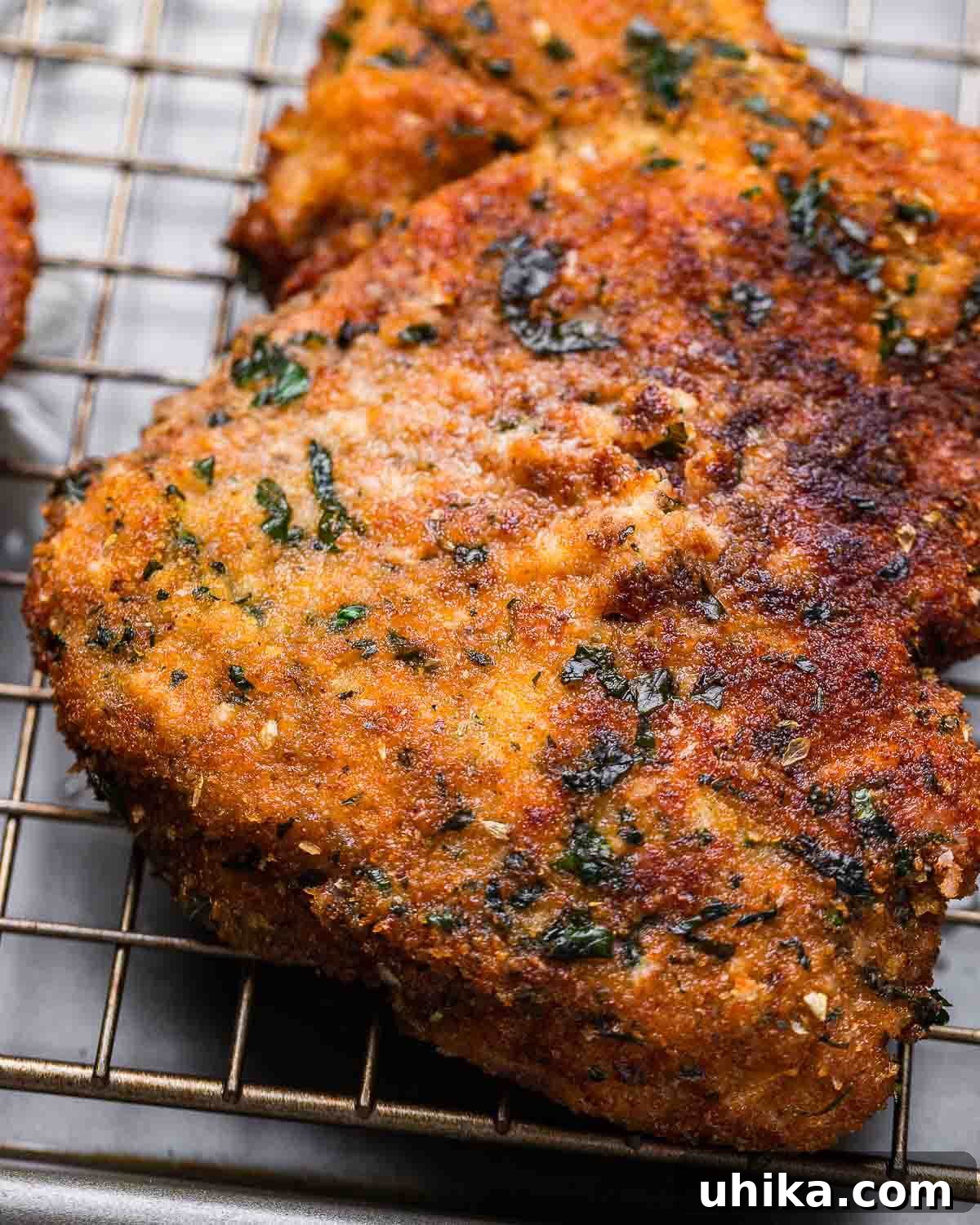 Crispy Milanese Pork Chops 5 Two freshly fried Pork Milanese cutlets resting on a wire rack, showing their golden-brown, crispy breading.