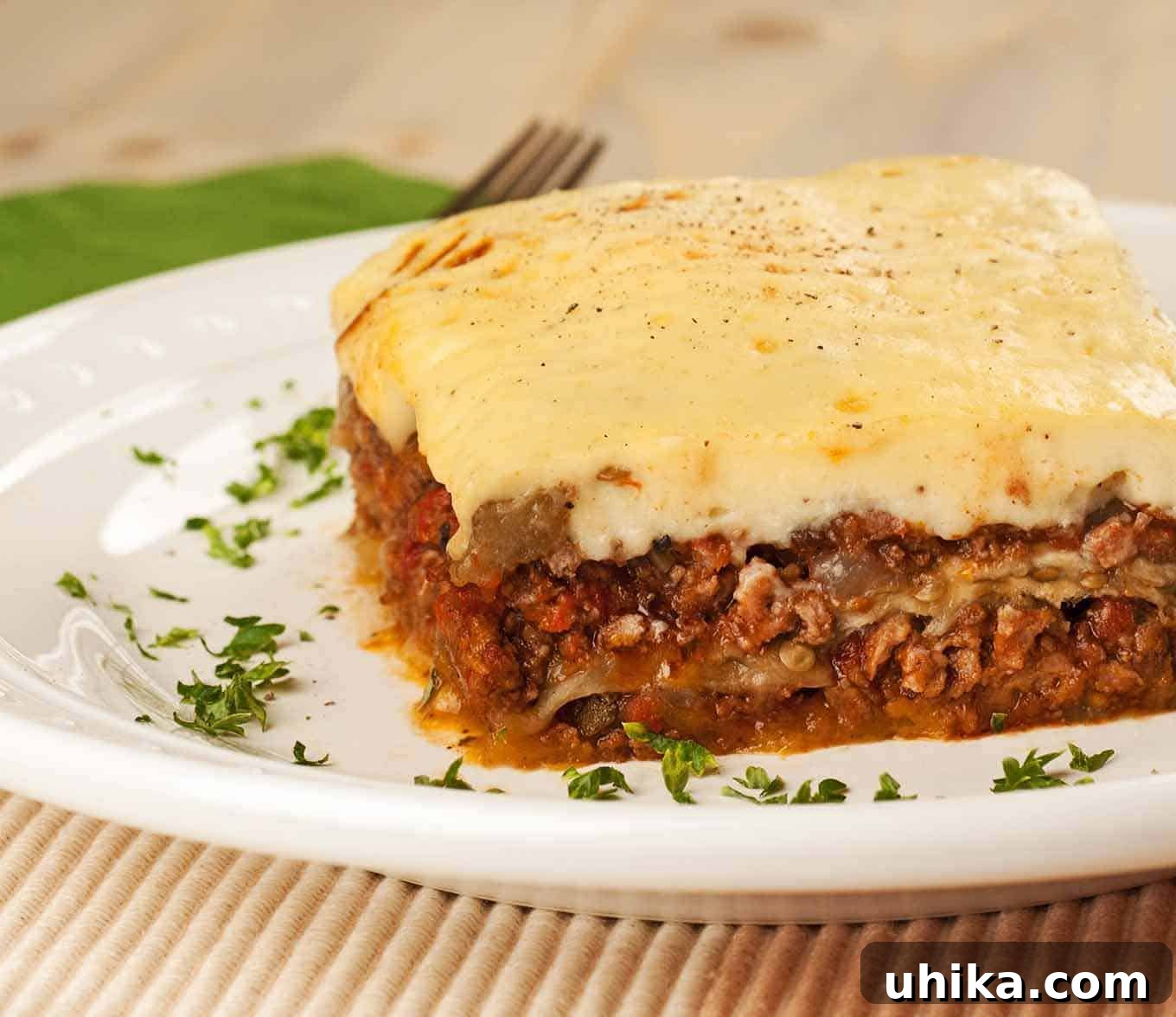 Classic Moussaka 2 A slice of traditional Greek moussaka made with ground lamb on a white plate, garnished with chopped parsley.