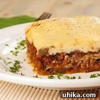 A small image of Moussaka, a slice made with ground lamb on a white plate, garnished with chopped parsley.