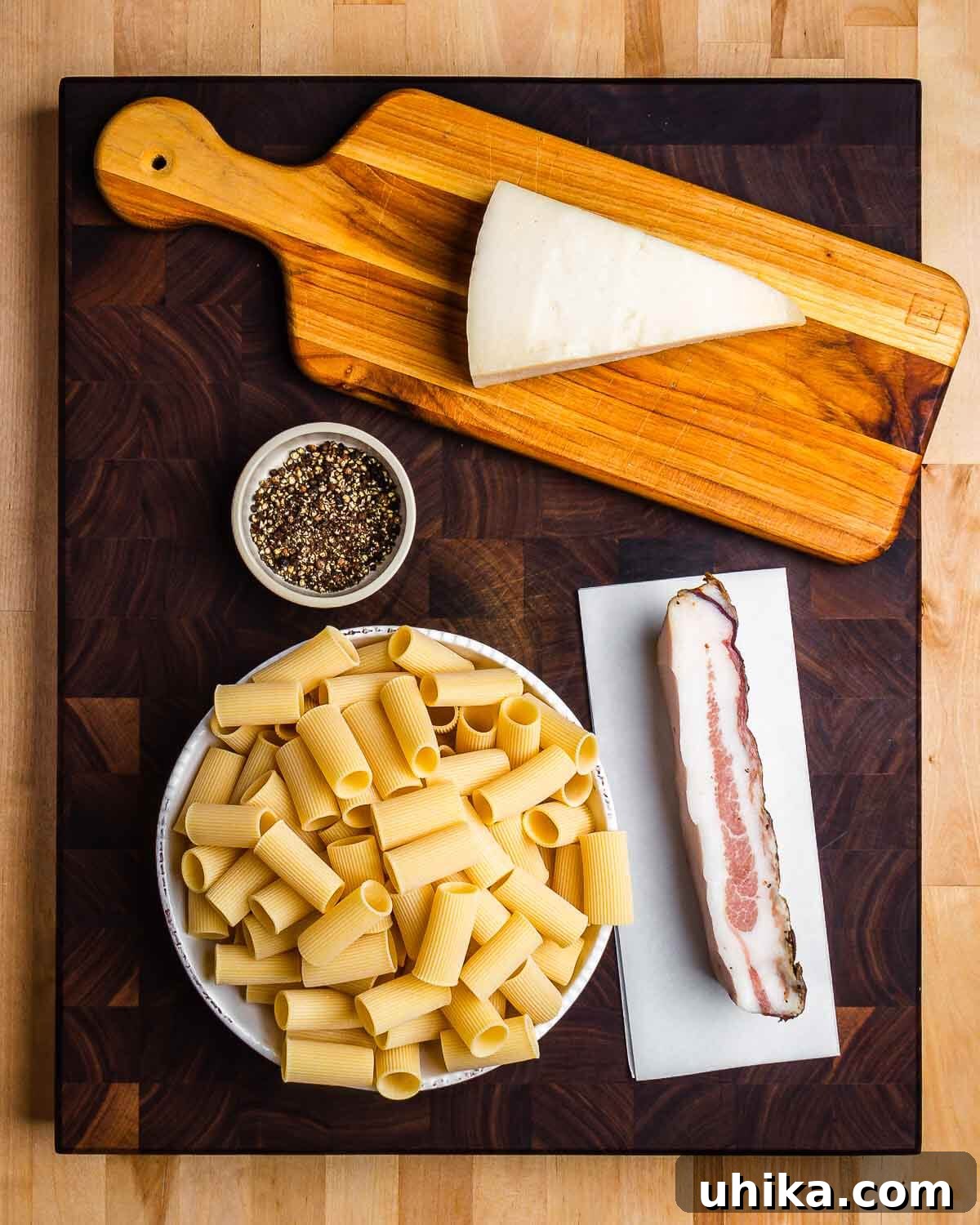 Roman Rigatoni with Cured Pork Cheek and Pecorino Cheese 3 Ingredients for Rigatoni alla Gricia: Pecorino Romano, black pepper, rigatoni, and guanciale laid out.