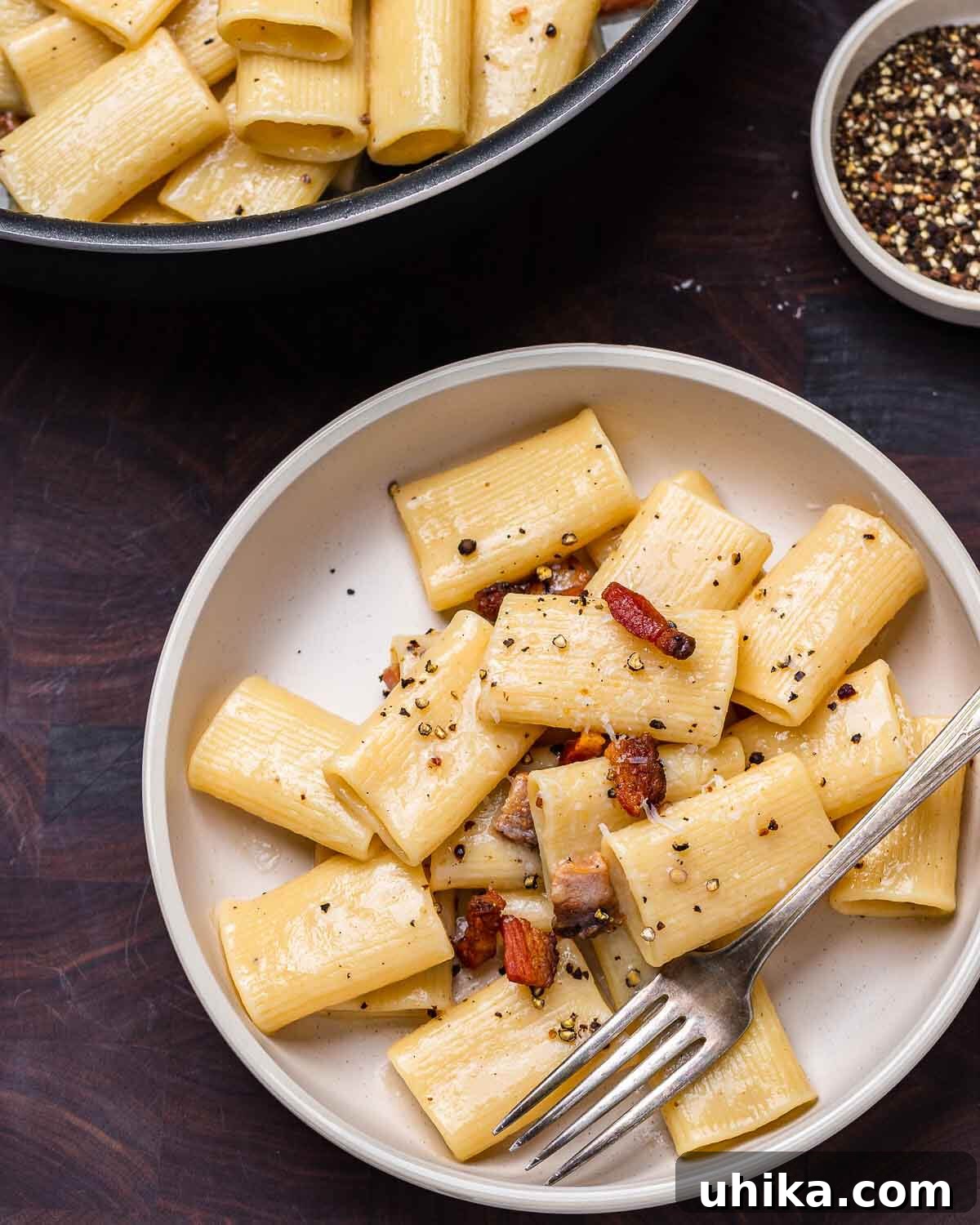 Roman Rigatoni with Cured Pork Cheek and Pecorino Cheese 9 White plate with rigatoni alla gricia on walnut cutting board, showing a perfectly sauced portion.