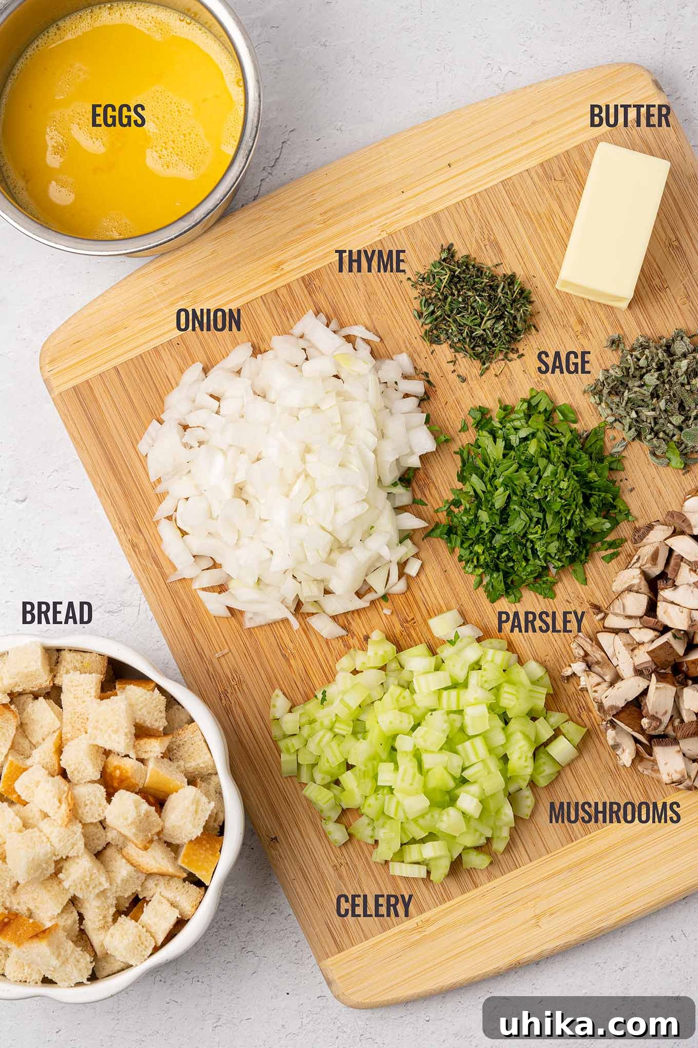 Heirloom Bread Stuffing 3 A labeled, overhead view of the ingredients for bread stuffing including bread cubes, eggs, butter, onion, celery, mushrooms, fresh thyme, parsley, and sage.