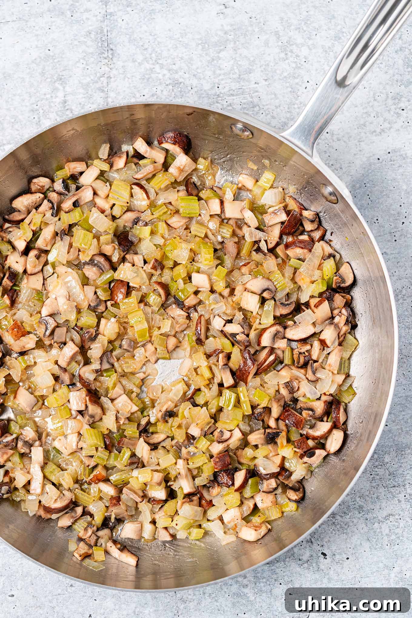 Heirloom Bread Stuffing 5 A frying pan filled with chopped onion, celery, and mushrooms sautéed in butter, ready to be added to homemade bread stuffing.